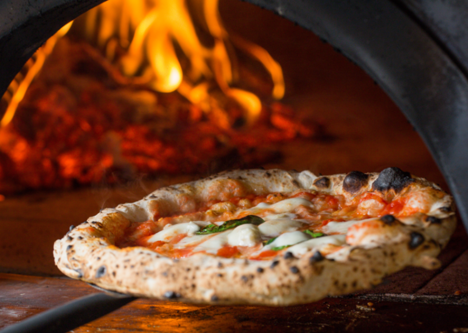 Margherita pizza being pulled out of pizza oven.