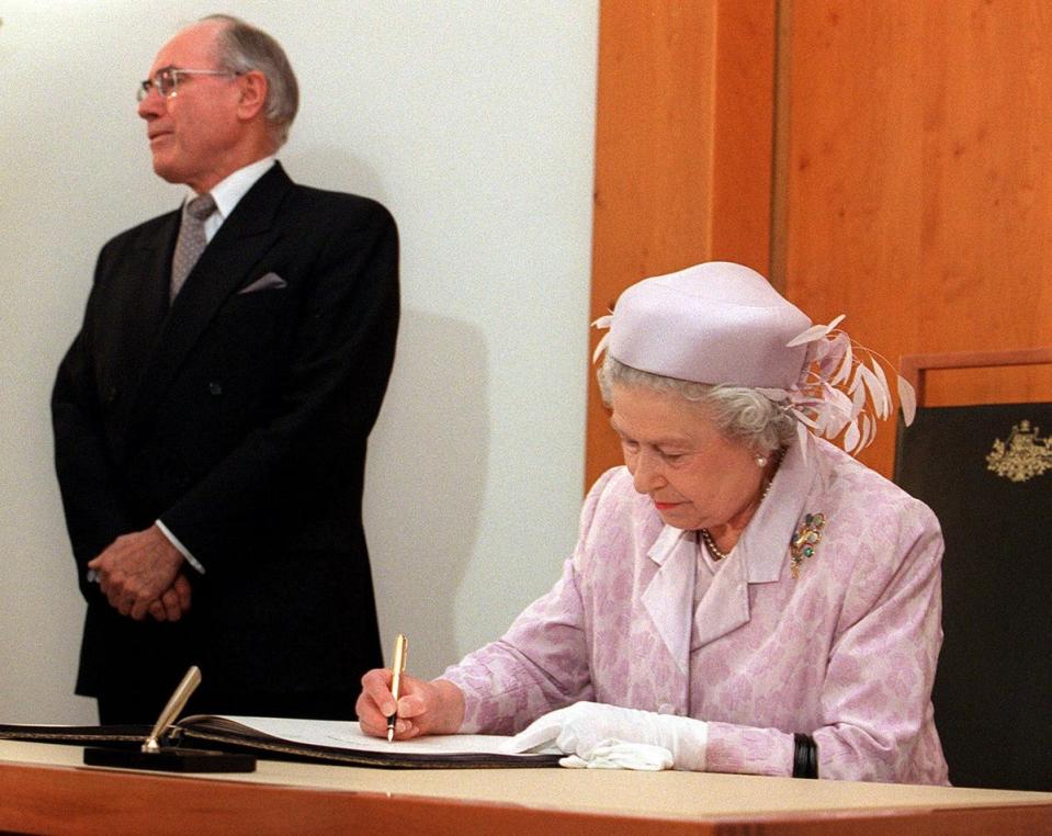 Queen Elizabeth II signs the visitor's book at Parliament House in Canberra 27 March 2000 as Australian Prime Minister John Howard stands in the background (NEWS LTD POOL/AFP via Getty Imag)