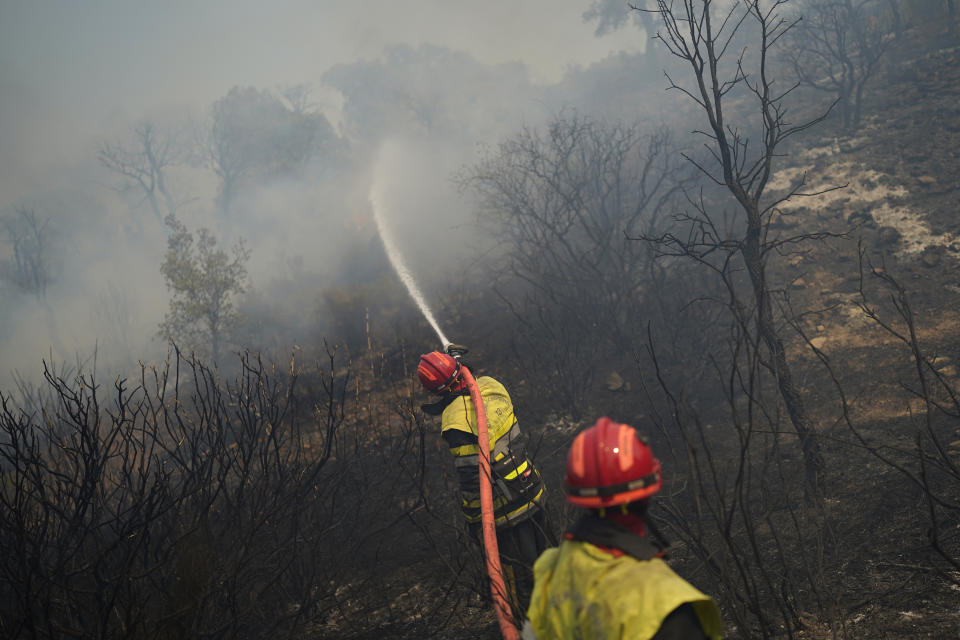 Firemen use a hose to extinguish a fire in a forest near Le Luc, southern France, Tuesday, Aug. 17, 2021. Thousands of people were evacuated from homes and vacation spots near the French Riviera as firefighters battled a fire racing through surrounding forests Tuesday, the latest of several wildfires that have swept the Mediterranean region.(AP Photo/Daniel Cole)