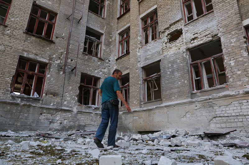 Local resident Andrey Butenko stands in front of the damaged school building where he lives in the basement in Lysychansk