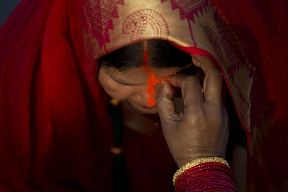 In this Saturday, Nov. 2, 2019, file photo, a Nepalese woman gets vermilion powder applied on her forehead after offering prayers to the setting sun at the Bagmati River during Chhath Puja festival in Kathmandu, Nepal. During Chhath, an ancient Hindu festival, rituals are performed to thank the sun god for sustaining life on earth. (AP Photo/Niranjan Shrestha, File)