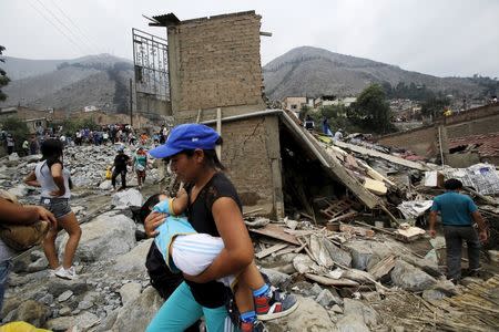 A woman carries a baby as she walks past debris of houses after a massive landslide in Chosica, March 24, 2015. REUTERS/ Mariana Bazo