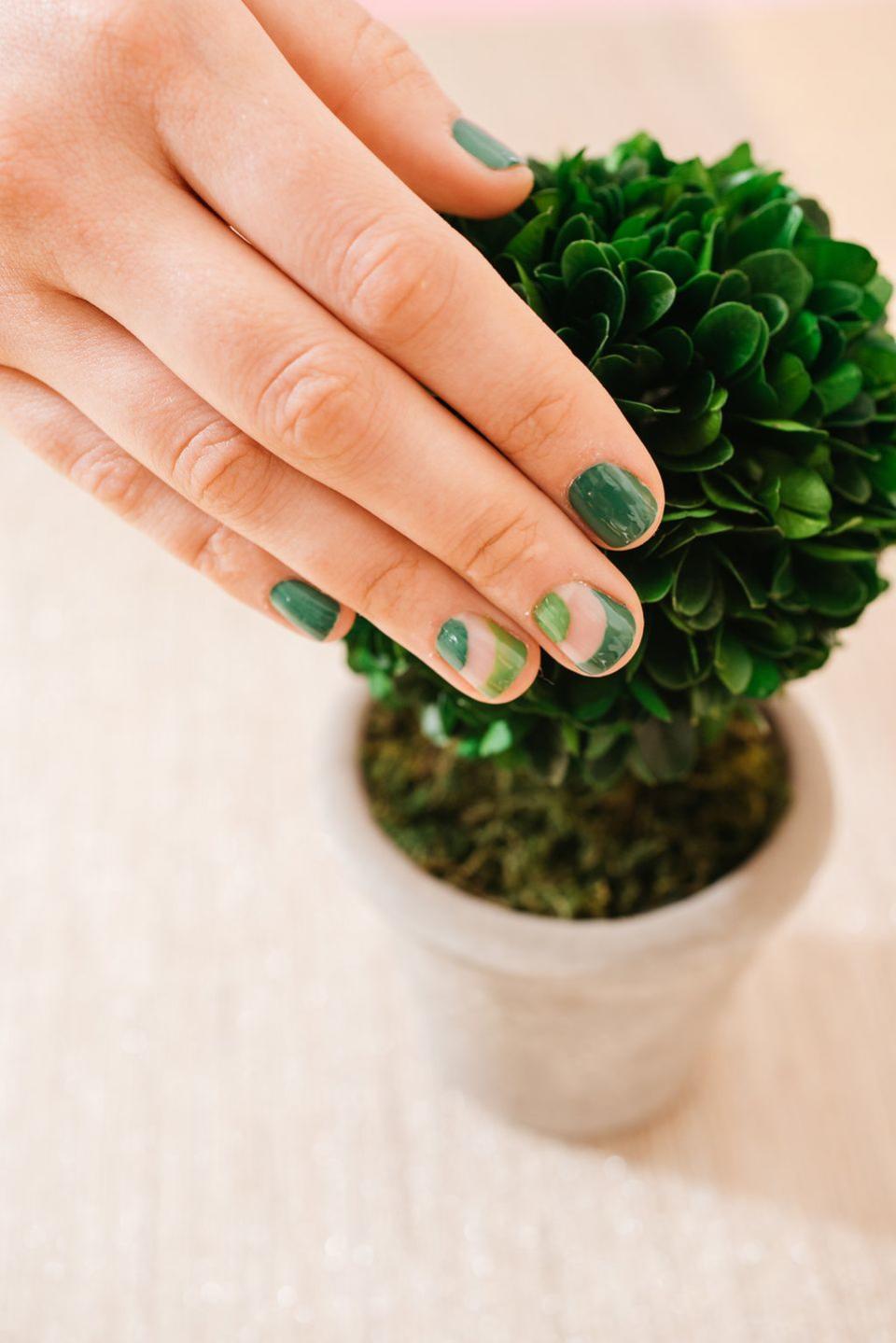 a female hand with green nail polish and a green plant in the background