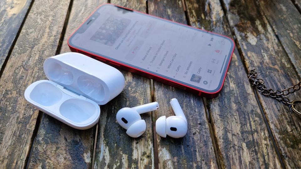 A pair of Apple AirPods Pro 2 lying on a table next to an open case and smartphone.