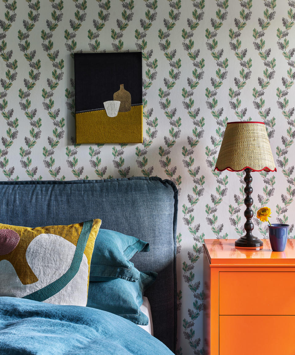 Bedroom with green, botanical wallpaper, blue bed with blue duvet cover, orange bedside table with table lamp