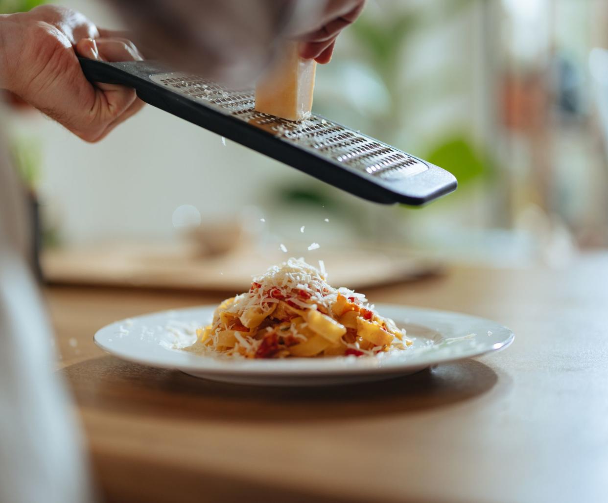 An anonymous chef in apron grating parmesan cheese in homemade pasta in the kitchen.