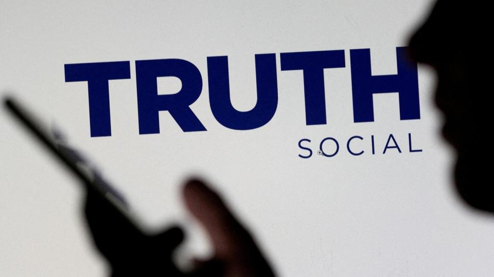 PHOTO: The Truth social network logo is seen displayed behind a woman holding a smartphone in this picture illustration, Feb. 21, 2022.  (Dado Ruvic/Reuters, FILE)