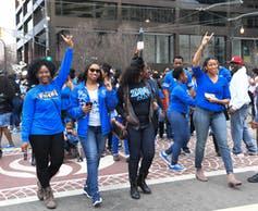 Several African American women dressed in blue walk together.