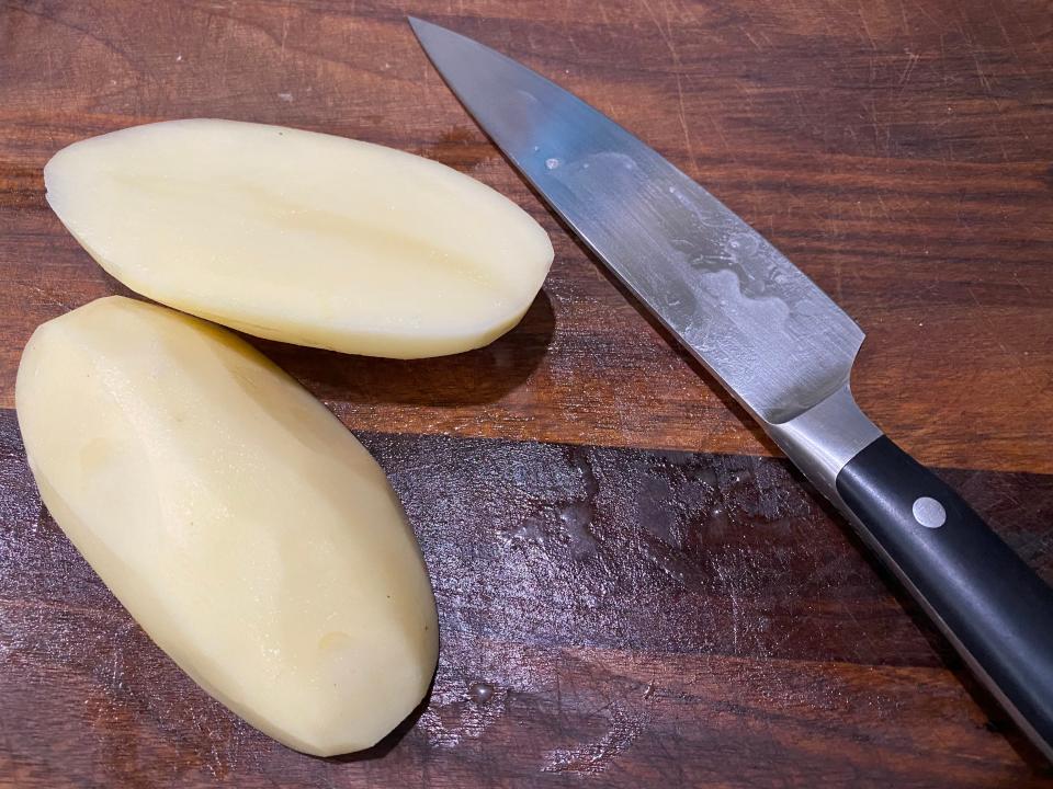 potato cut in half on a cutting board next to a knife