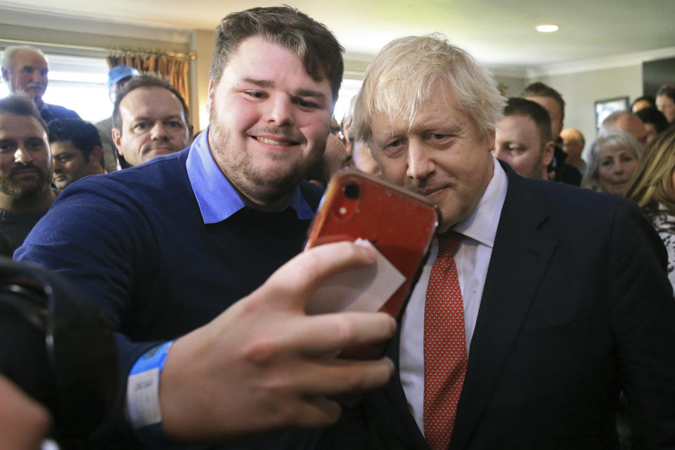 Britain's Prime Minister Boris Johnson poses for a selfie with a supporter, during a visit to Sedgefield Cricket Club in County Durham, north east England, Saturday Dec. 14, 2019, following his Conservative party's general election victory.  Johnson called on Britons to put years of bitter divisions over the country's EU membership behind them as he vowed to use his resounding election victory to finally deliver Brexit. (Lindsey Parnaby/Pool via AP)