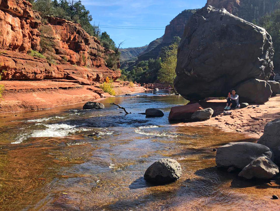 In this 2018 photo a visitor sits near Oak Creek in Slide Rock State Park near the town of Sedona, Ariz. The sleepy Arizona town of Sedona has long been a refuge for hikers, romantics and soul searchers. There’s picturesque beauty in its earth-toned buildings and also in the glowing red rocks that surround town. And many visitors come looking for something besides this beauty: the so-called vortex where some say the earth’s energy crackles and creates sensations of healing and spiritual awakening. (AP Photo/Joseph Gedeon)