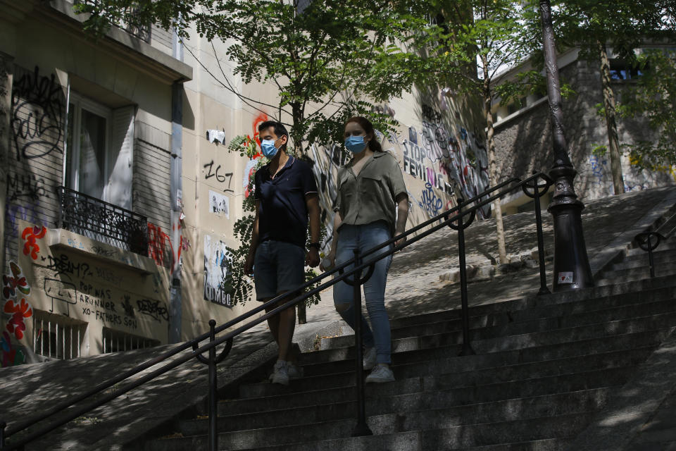 A couple walk down the stairs in the Montmartre district Monday, Aug. 10, 2020 in Paris. People are required to wear a mask outdoors starting on Monday in the most frequented areas of the French capital. The move comes as the country sees an uptick in virus infections. (AP Photo/Michel Euler)