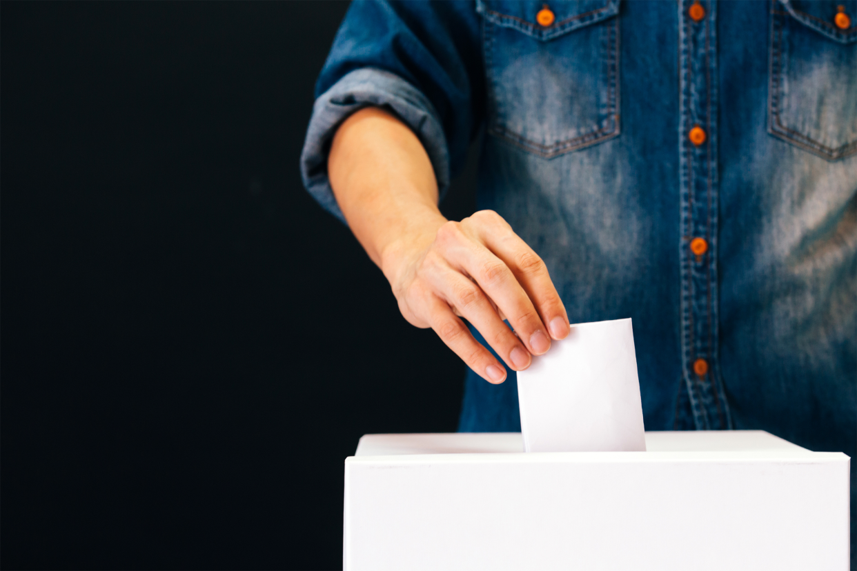 person putting piece of paper in a ballot box