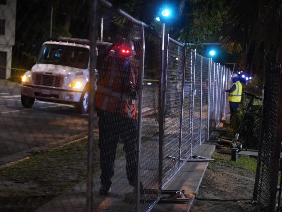 Los Angeles city contractors install a temporary fence around Echo Park Lake's perimeter in Los Angeles early Thursday, March 25, 2021. Los Angeles Police officers sweep managed to corral demonstrators gathered Wednesday to protest the planned closure of a Los Angeles park that would displace a large homeless encampment that has grown throughout the coronavirus pandemic. The park will be closed for repairs.(AP Photo/Damian Dovarganes)