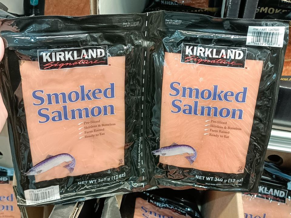 Hand holding a black and clear two-pack of smoked salmon at Costco