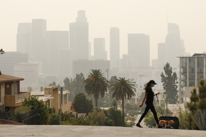 LOS ANGELES, CA - SEPTEMBER 14: Breya Hodge walks her dog &quot;Sophie&quot; as smoke and ash from the Bobcat fire burning in the Angeles National Forest have blanketed the region for a week, contributing to poor air quality which nearly obscures the tall buildings of downtown Los Angeles September 14, 2020. Current air quality readings are considered unhealthy for sensitive groups according to the Environmental Protection Agency. The bobcat fire is one of more than 25 fires burning in California creating a plume that spanned more than 1,000 miles. Downtown on Monday, Sept. 14, 2020 in Los Angeles, CA. (Al Seib / Los Angeles Times