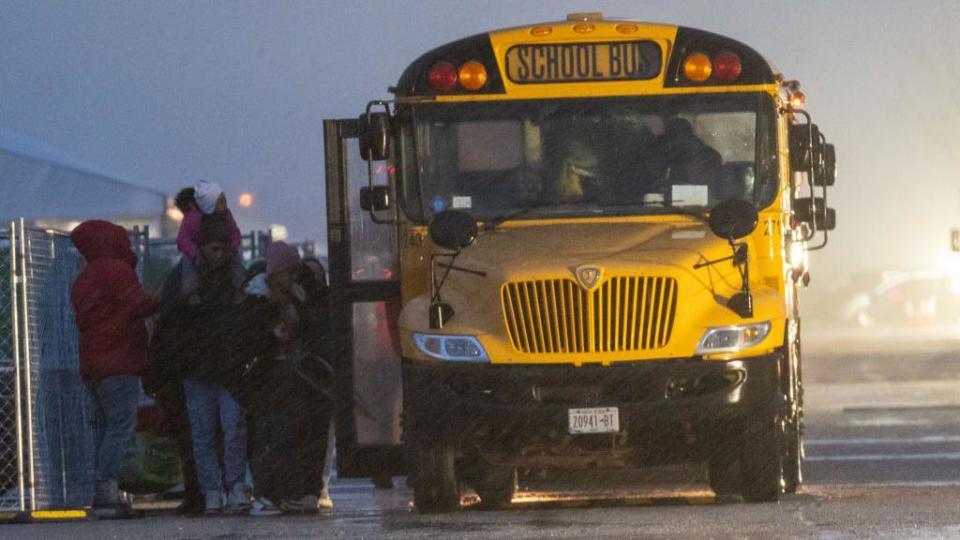 Unos migrantes hacen fila para subir a un autobús escolar que los llevará de Floyd Bennett Field a un instituto local donde protegerse de la tormenta en enero de 2024, en Brooklyn, Nueva York, Estados Unidos.imated wind speeds to be more than 70 mph. on January 09, 2024 in the Brooklyn borough of New York City.