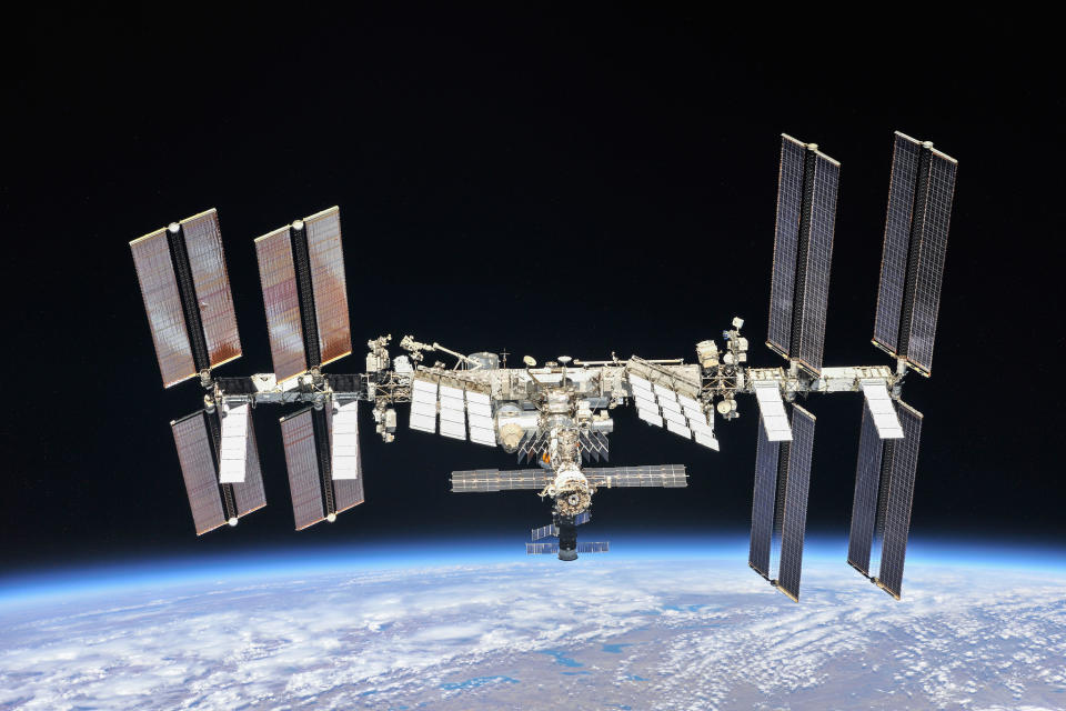 a large H-shaped space station with wing-like solar panels floats above a blue-white Earth