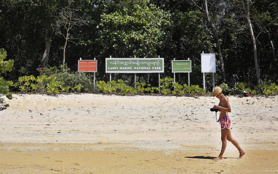 In this Feb. 10, 2014 photo, a Thai tourist walks on a beach along Lampi Marine National Park on Lampi Island, Myanmar. Off a remote, glimmering beach backed by a lush tropical forest, environmental project manager Julia Tedesco skims the crystalline waters with mask and fins, looking for coral and fish life. “There is almost nothing left down there,” Tedesco says, wading toward a sign planted on the shore reading “Lampi National Park.” (AP Photo/Altaf Qadri)