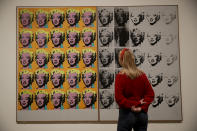 A Tate representative poses for photographs next to the 1962 Andy Warhol piece "Marilyn Diptych" during a media preview for the exhibition "Andy Warhol" at the Tate Modern gallery in London, Tuesday, March 10, 2020. The exhibition, which runs from March 12 to September 6, features over 100 works spanning the American artist's career in the second half of the 20th century until his death in 1987. (AP Photo/Matt Dunham)