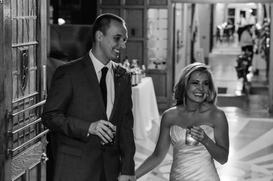 Black and white image of the author (right) and her husband on their wedding day, smiling and walking down the hall of their wedding venue