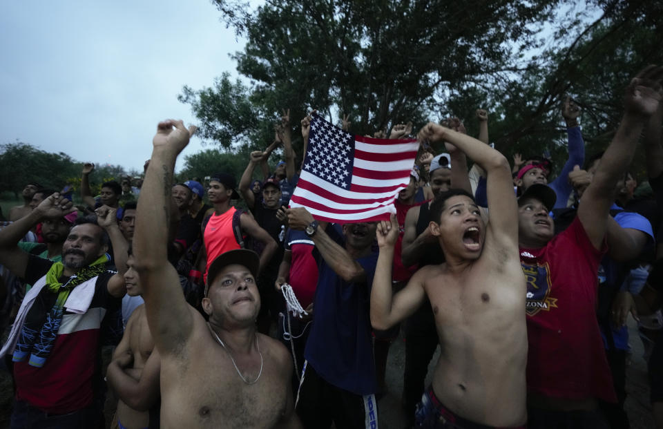 FILE - Venezuelan migrants wave a U.S. flag at a television helicopter that flew over the Rio Grande, in Matamoros, Mexico, on May 12, 2023, a day after pandemic-related asylum restrictions called Title 42 were lifted. President Joe Biden has ordered a halt to asylum processing at the U.S. border with Mexico when arrests for illegal entry top 2,500 a day, which was triggered immediately. (AP Photo/Fernando Llano, File)