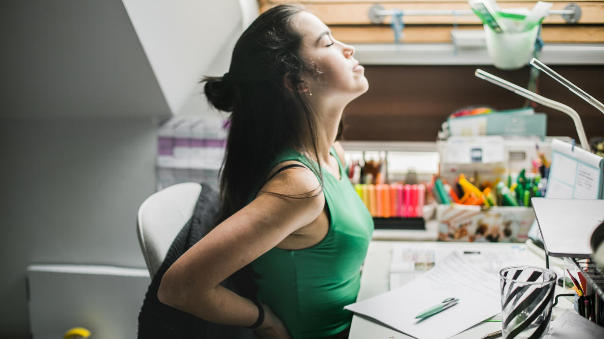  A woman feels her back as she sits at a desk. . 