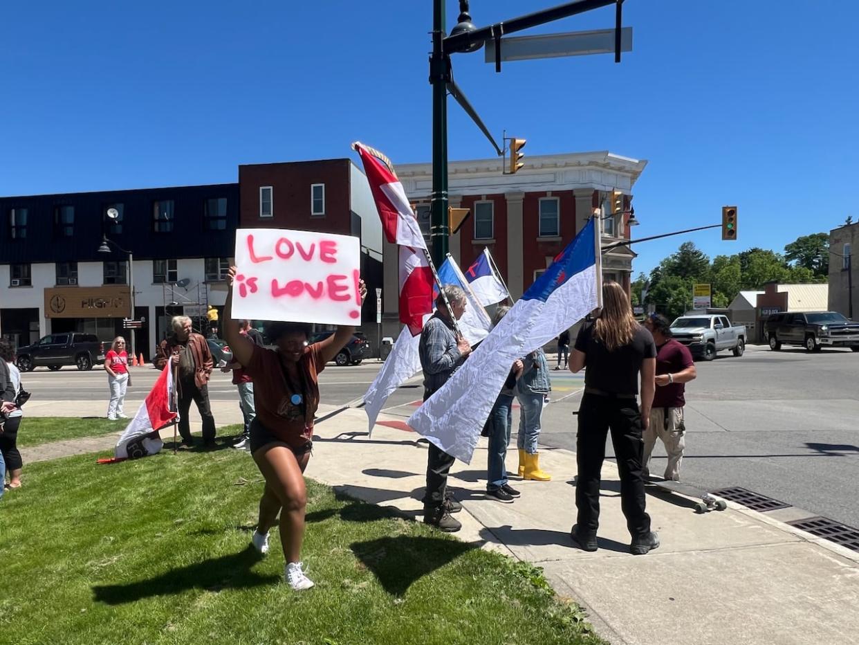 A Pride supporter with a sign walks past a group opposed to the flag-raising event in Ingersoll, Ont., on Friday. (Andrew Lupton/CBC - image credit)