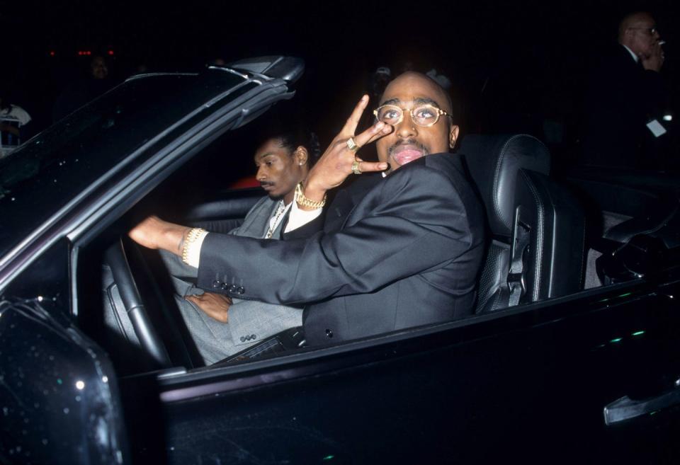 tupac and close friend, snoop dogg, pull up at the 23rd annual american music awards in 1996 in a drop top car pulling gang signs