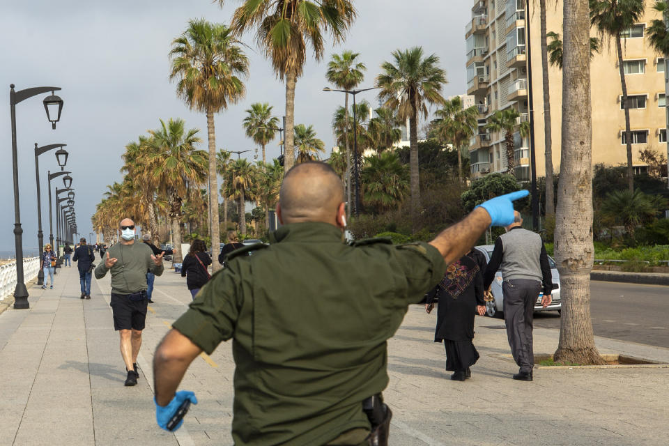 A municipal policeman, center, orders people to evacuate the corniche, or waterfront promenade, along the Mediterranean Sea, as the country's top security council and the government were meeting over the spread of coronavirus, in Beirut, Lebanon, Sunday, March 15, 2020. Lebanon has been boosting precautionary measures including halting flights from several countries, closing all restaurants and nightclubs and tightening measures along the border with neighboring Syria. (AP Photo/Hassan Ammar)