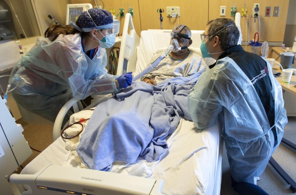 Chaplain Kevin Deegan, right, kneels as nurse Cristina Marco listens to Domingo Benitez, 70, inside the COVID unit.