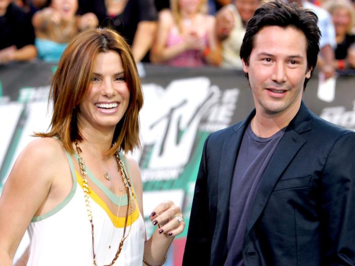 Sandra Bullock and Keanu Reeves smiling at a red carpet event together.