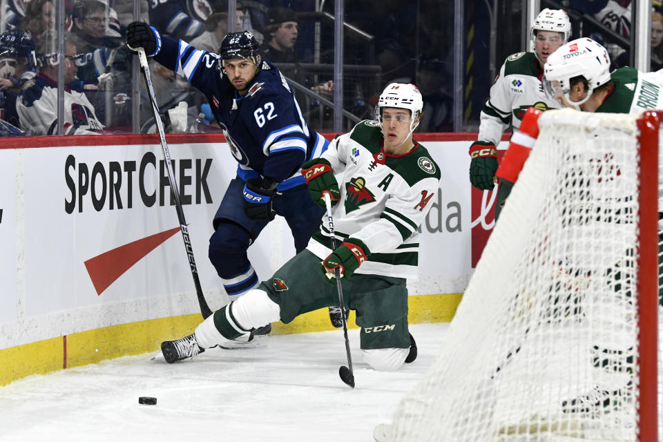 Minnesota Wild's Joel Eriksson Ek (14) passes the puck behind the net as he is checked by Winnipeg Jets' Nino Niederreiter (62) during the second period of an NHL hockey game Tuesday, Feb. 20, 2024, in Winnipeg, Manitoba. (Fred Greenslade/The Canadian Press via AP)