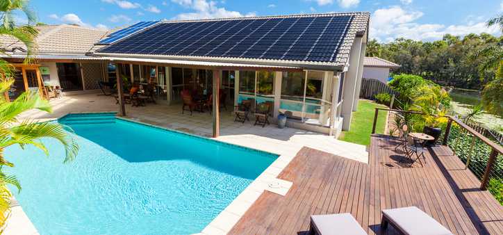 A house with solar panels on the roof overlooking a pool in a back yard.