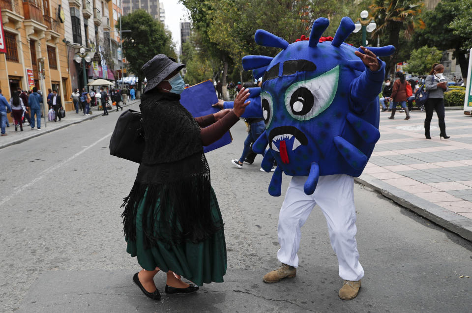 Un policía vestido con un traje que representa el virus COVID-19 intenta abrazar a un peatón, que se resiste, en el Paseo El Prado como parte de una campaña de concientización sobre la propagación del nuevo coronavirus en La Paz, Bolivia, el miércoles 10 de febrero de 2021. (AP Foto/Juan Karita)