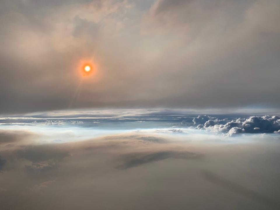 A whispy pyrocumulonimbus cloud is seen in the foreground from above as the sun in the background filtered through smoke