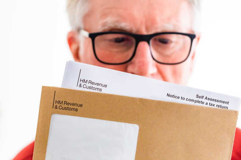 Senior man opening a tax letter from HMRC in a brown envelope. Focus on the letter with the man defocused in the background.