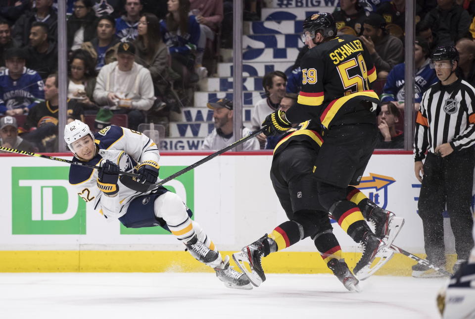 Buffalo Sabres' Brandon Montour, left, is tripped by Vancouver Canucks' Jay Beagle, back right, as Canucks' Tim Schaller (59) tries to avoid colliding with them during the second period of an NHL hockey game in Vancouver, British Columbia, Saturday, Dec. 7, 2019. (Darryl Dyck/The Canadian Press via AP)