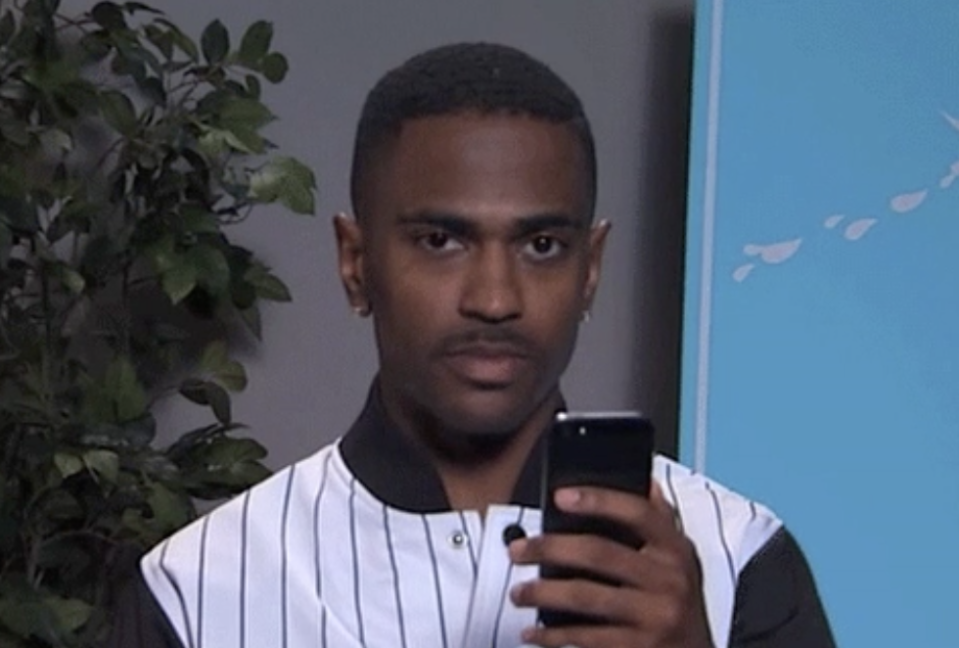 Big Sean holding a phone and looking directly at the camera with judgment