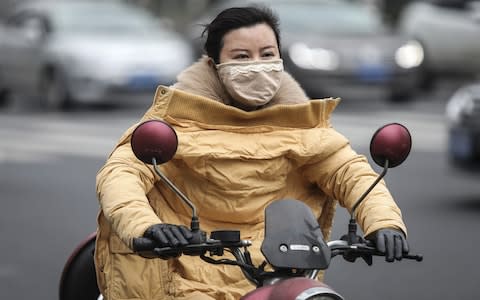 A woman wears a mask while riding an electric bicycle  - Credit: Getty