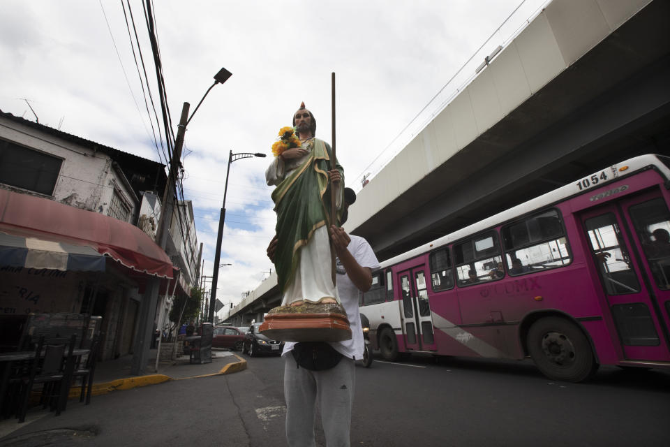 A devotee seeking alms holds a statue of Saint Judas near the site where an elevated section of the subway Line 12 collapsed in early May killing 26 people, in Mexico City, Thursday, June 17, 2021. Residents who once depended on Line 12 are now obligated to find an alternative way to commute. (AP Photo/Marco Ugarte)