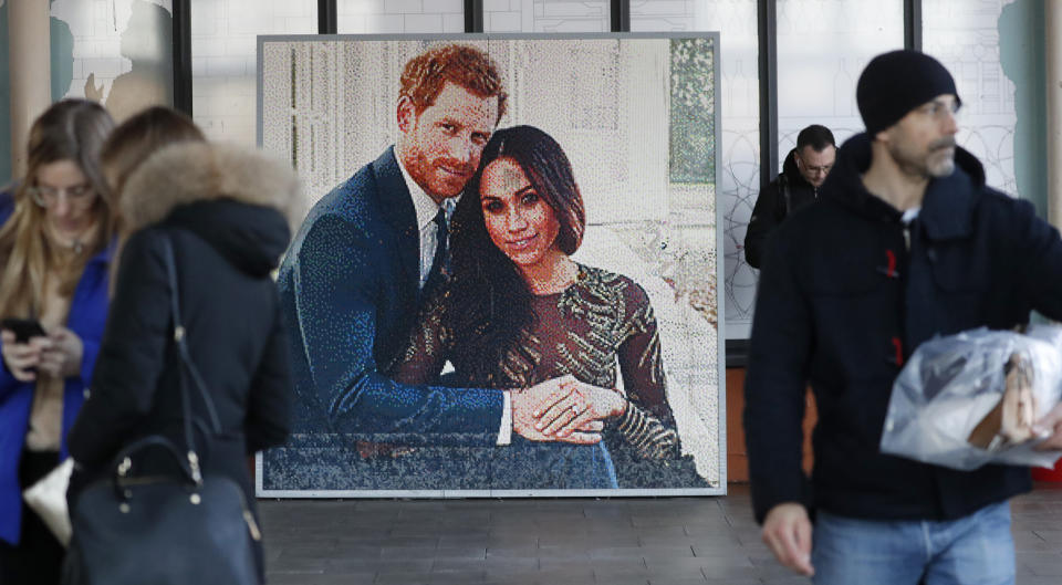 People walk past a picture of Britain's Prince Harry and Meghan Duchess of Sussex, in Windsor, Friday, Jan. 10, 2020. Britain's Prince Harry and his wife, Meghan, said they are planning "to step back" as senior members of the royal family and "work to become financially independent." (AP Photo/Frank Augstein)