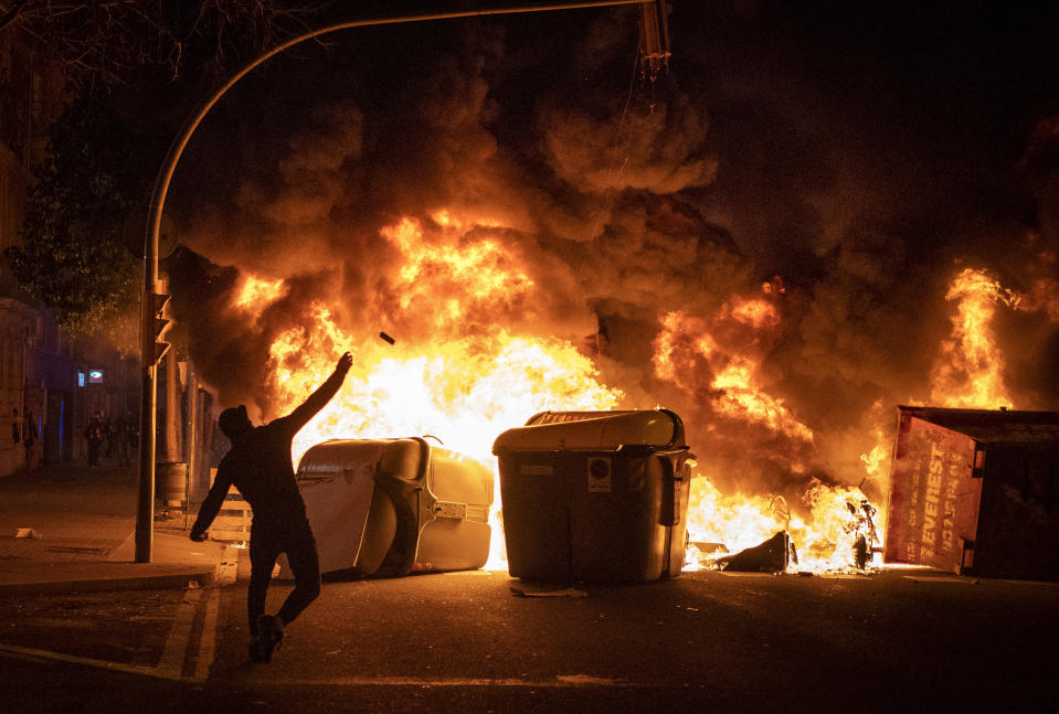 A demonstrator throws a stone against police during clashes following a protest condemning the arrest of rap singer Pablo Hasel in Barcelona, Spain, Thursday, Feb. 18, 2021. The imprisonment of Pablo Hasel for inciting terrorism and refusing to pay a fine after having insulted the country's monarch has triggered a social debate and street protests. (AP Photo/Emilio Morenatti)