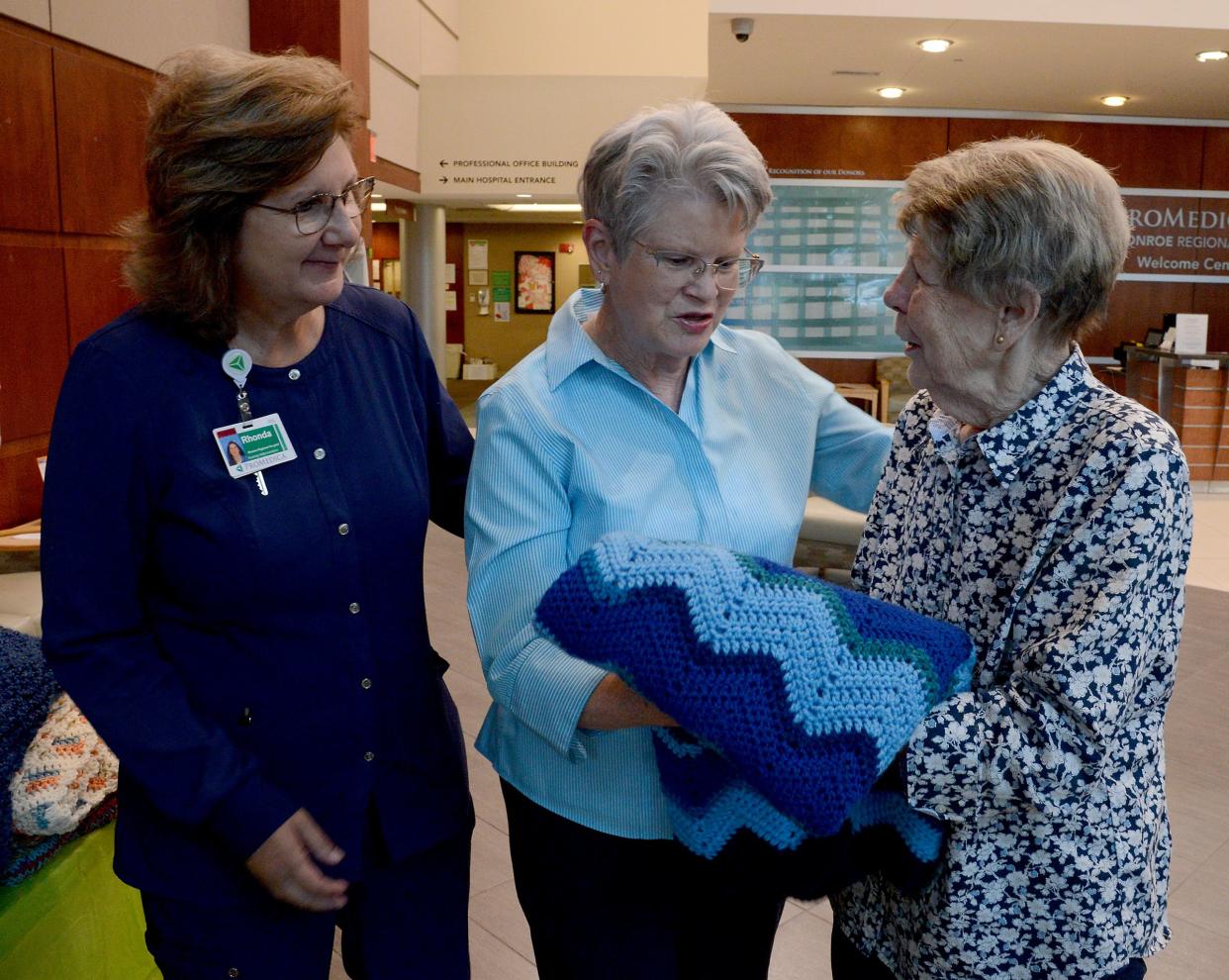 Rhonda Witte RN, MSN director of medical oncology at ProMedica Monroe observes as auxiliary member Sharon Leader gives a handmade lap robe to Diana Molenda at a presentation Wednesday, June 26, 2024 at ProMedica Monroe Regional Hospital.