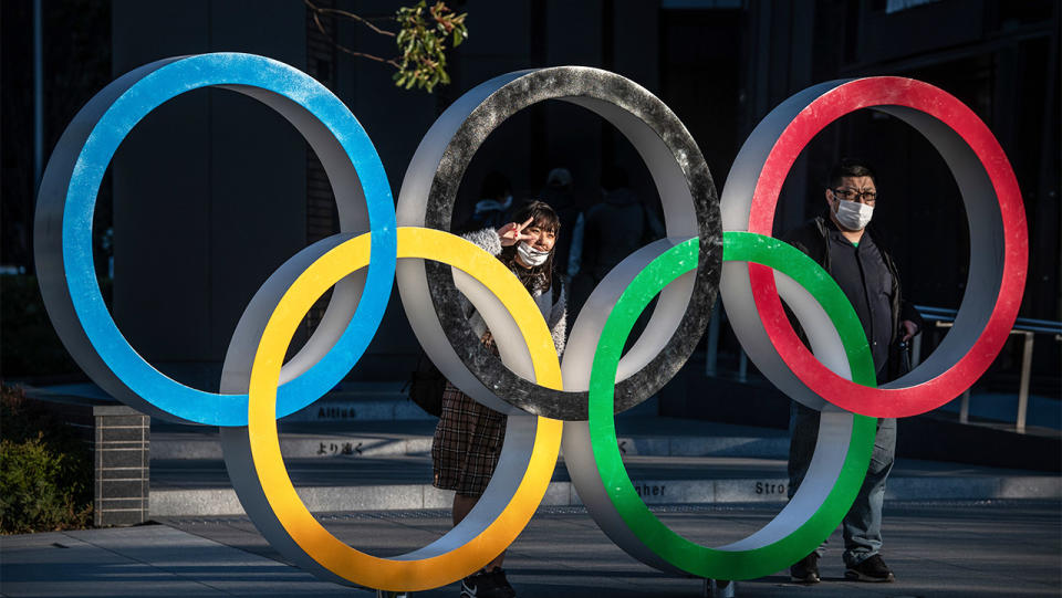 People wearing face masks pose for photographs next to Olympic Rings in Japan.