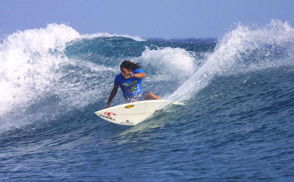 Tamayo Perry wearing a blue rash guard and surfing in Tahiti