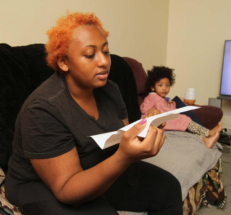 Jasmine Kirk reads a notice from her apartment's management that she is late on her rent payment as she sits in her home with her daughter, Luna, in Akron.