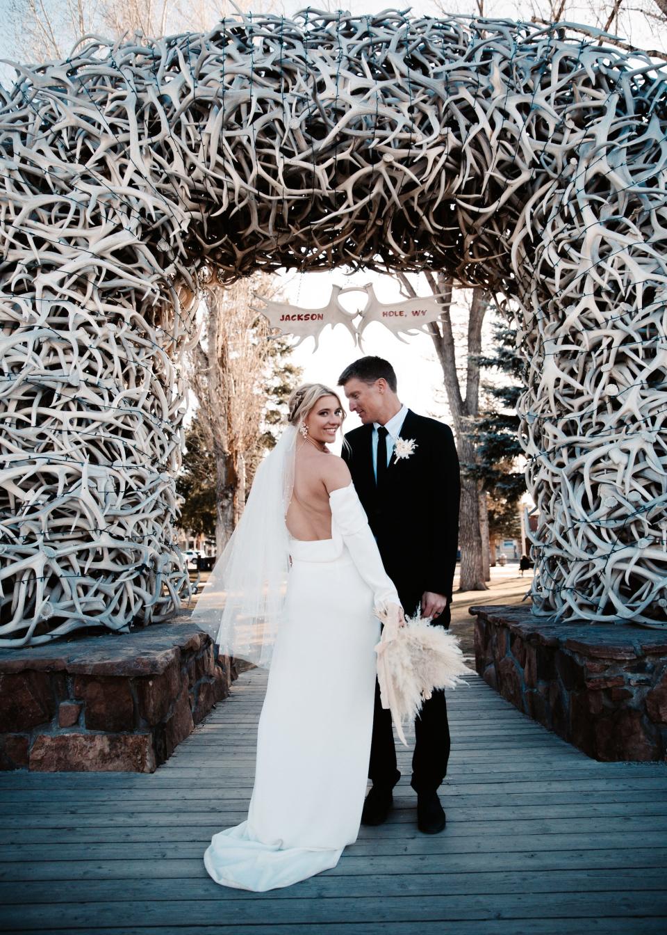 A bride looks over her shoulder in front of an archway as her groom looks at her.
