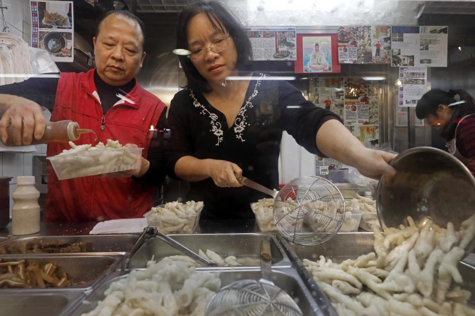 In this Monday, Jan. 23, 2017 photo, chicken feet snacks shop owner Leung Kin-kung, left, and his wife Leung pack chicken feet takeaway for customer in Hong Kong. Saturday marks the start of the lunar Year of the Rooster and families in China will reunite for festivities, fireworks and food. While tradition calls for feasting on “auspicious” foods, many will also munch on staple snacks like “phoenix claws,” the Chinese name for chicken feet. (AP Photo/Vincent Yu)