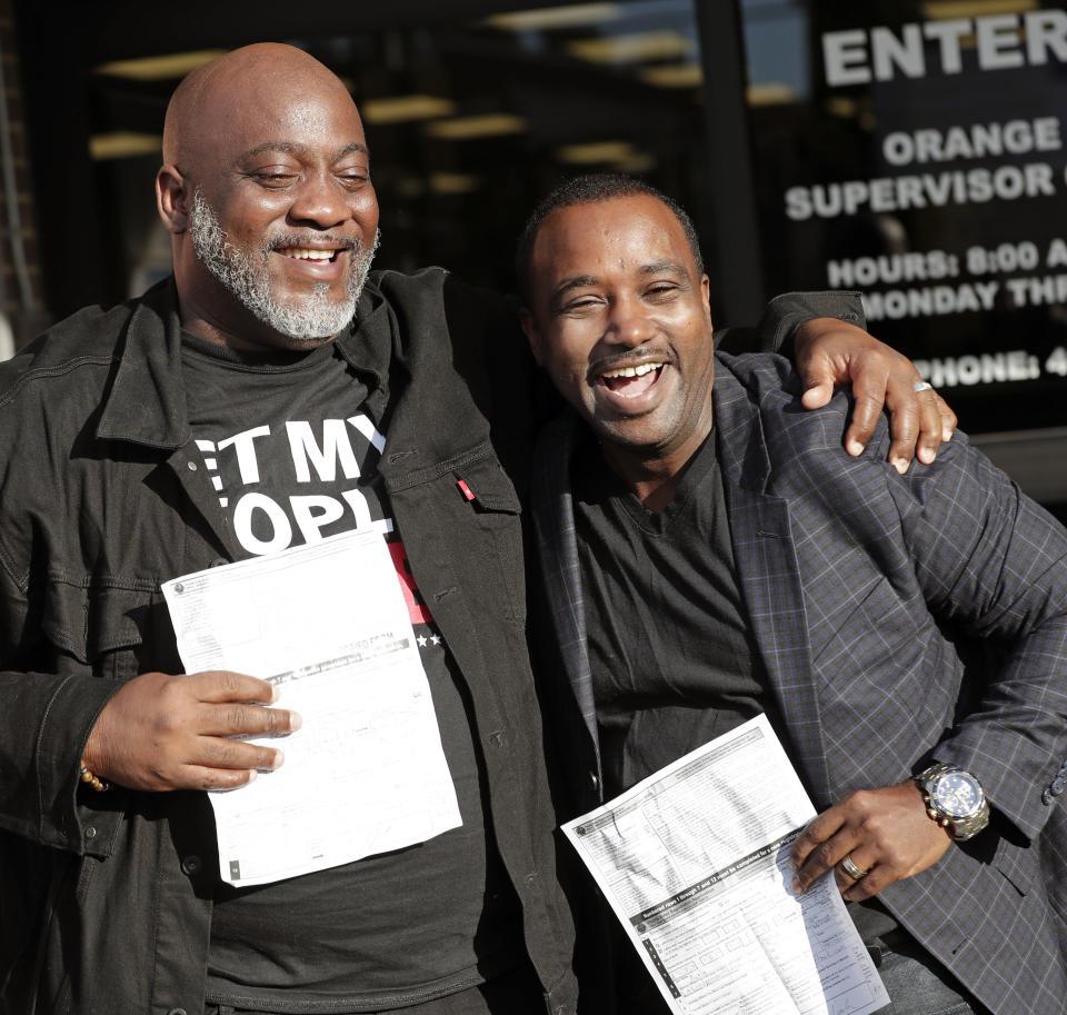 Desmond Meade, looking thrilled, puts his arm around David Ayala, who is shouting with joy. Each is holding a form.